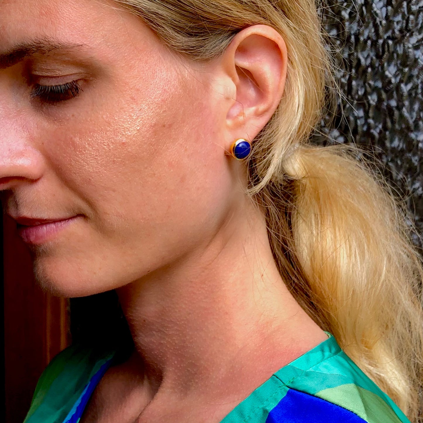 Close-up of a woman wearing blue lapis lazuli stud earrings gold with a blurred background