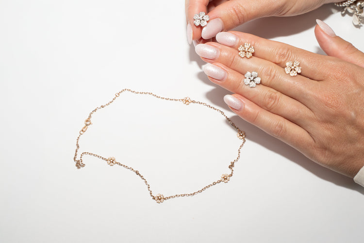 Hand holding a delicate flower earrings and necklace out of gold with diamonds