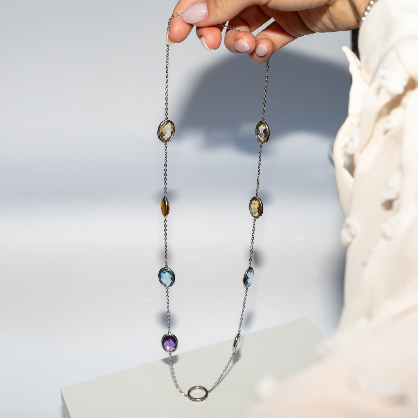 Colorful Necklace Oval Gemstones set in white gold with hand on light grey background