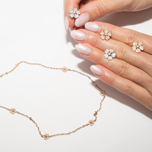 Hand holding a delicate flower earrings and necklace out of gold with diamonds