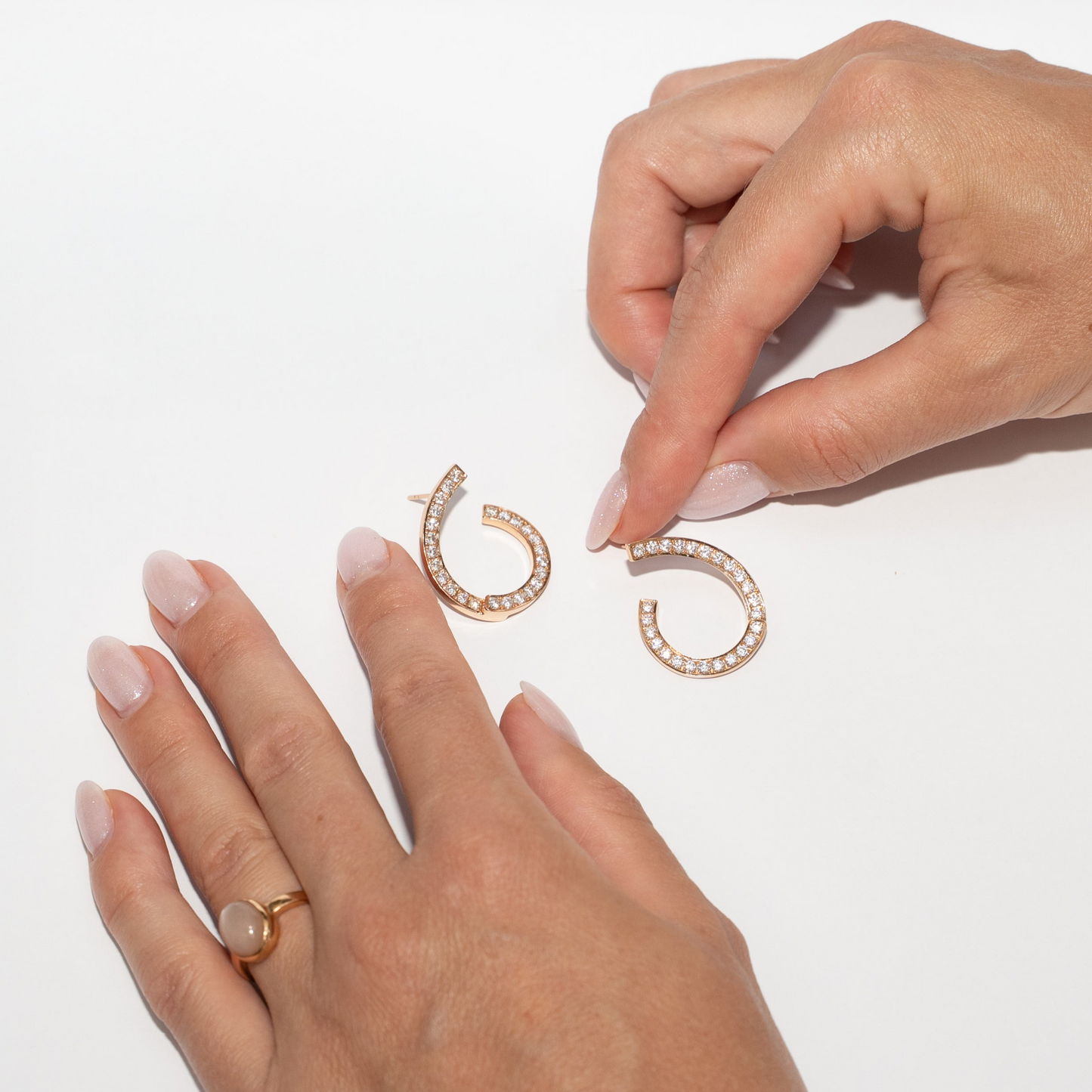 Rose gold hoop earrings with diamonds on a white background with hands